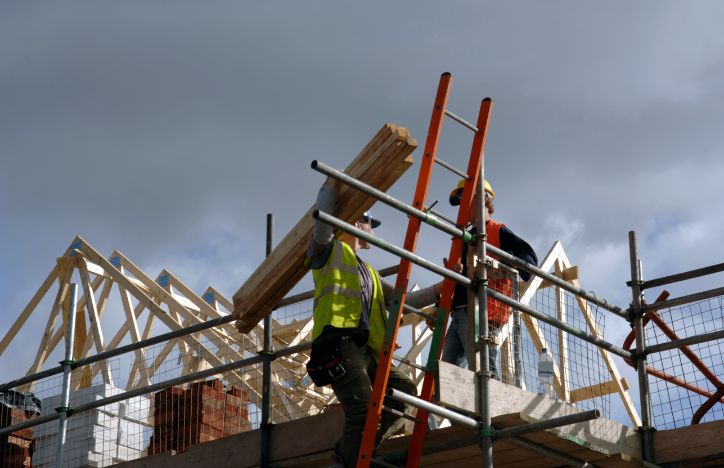 Low View Of Two Construction Workers On Top Of House Frame