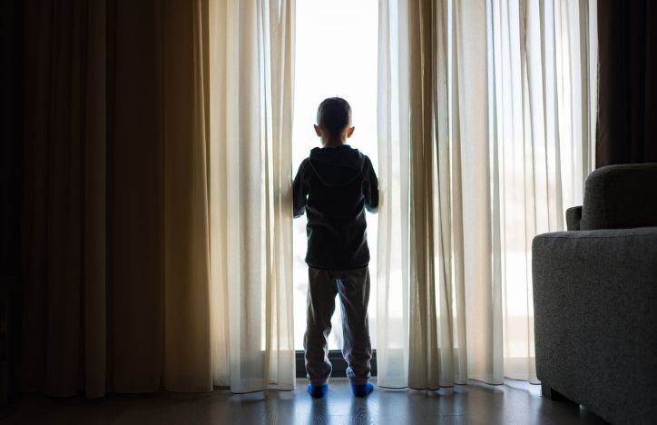 Young Boy Looking Out Of The Window Of His Home