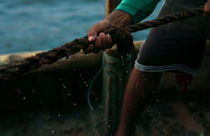 A Close Up Of A Hand Gripping A Wet, Textured Rope On A Boat, With Water Droplets In Focus
