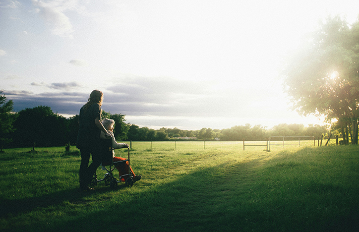 A Woman And A Girl In A Wheelchair Looking At The Sunrise In A Field