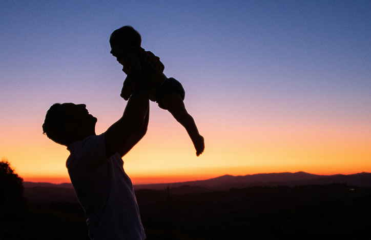 Parent Holding Child Above Their Head Infront Of A Sunset