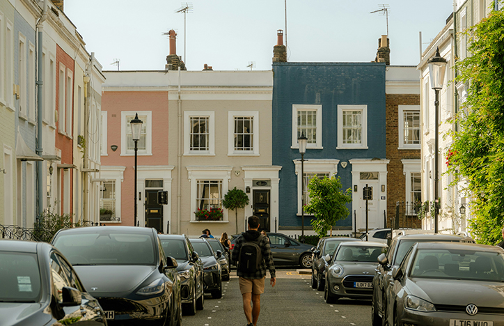 A Man Walking Down A Street In London To Colourful Houses