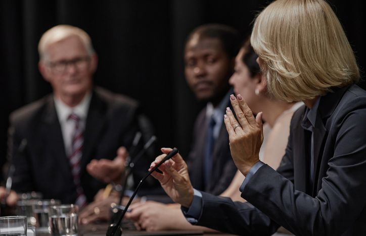 Public Inquiry A Woman Speaking Into A Microphone While Other Representatives Listen On
