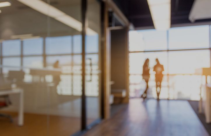 Two Business Partners Standing By A Window At The End Of An Office Hallway