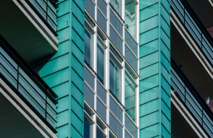 Close Up Of A Modern Building Facade With Turquoise Cladding And Glass Windows.